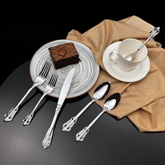 Silver cutlery set on a table with a plate of cake and a cup.